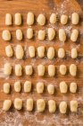 Сверху вид на непрожаренные клецки, расставленные в организованных рядах на деревянном столе во время приготовления обеда дома — стоковое фото