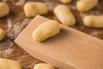 Top view of pieces of soft raw dough placed on wooden table covered with flour near ribber board during gnocchi preparation in the kitchen — Stock Photo