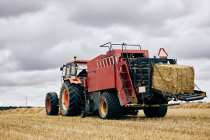Rollo de heno seco y tractor moderno colocado en el campo agrícola en la zona montañosa en verano - foto de stock