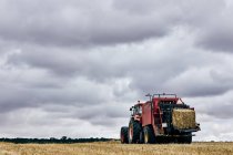 Getrocknete Heurolle und moderner Traktor im Sommer auf landwirtschaftlichem Feld im Gebirge — Stockfoto