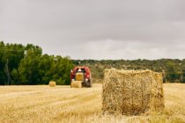 Rolo de feno seco e trator moderno colocado no campo agrícola na área montanhosa no verão — Fotografia de Stock