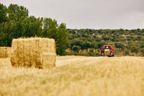 Rouleau de foin séché et tracteur moderne placé sur un champ agricole en zone montagneuse en été — Photo de stock