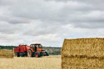 Getrocknete Heurolle und moderner Traktor im Sommer auf landwirtschaftlichem Feld im Gebirge — Stockfoto