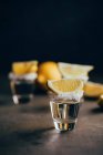 Tiros de tequila con sal y limón colocados sobre superficie reflectante sobre fondo oscuro - foto de stock