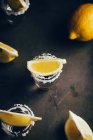 Vista superior de tiros de tequila con sal y limón colocados sobre una superficie rústica sobre fondo oscuro - foto de stock