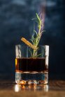 Glass of whiskey with rosemary placed on wooden table against blue background — Stock Photo