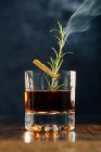 Bicchiere di whisky con rosmarino appoggiato su tavolo di legno su sfondo blu — Foto stock
