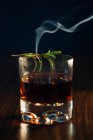 Glass of whiskey with rosemary placed on wooden table against blue background — Stock Photo