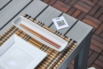 De arriba del pedazo de papel con el código QR del menú puesto a la mesa con los palillos y el plato en el restaurante asiático - foto de stock