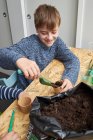 Щаслива дитина з садовою лопатою, заповнюючи еко чашку з землею за столом — стокове фото