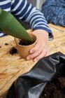 Crop anonymous kid with gardening shovel filling eco cup with earth at table — Stock Photo