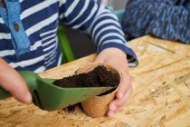 Crop anonymous kid with gardening shovel filling eco cup with earth at table — Stock Photo