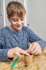 Contenu enfant plantant des semis verts dans une tasse en carton avec de la terre à table dans la maison pendant la journée — Photo de stock