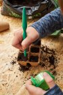 From above of crop anonymous kid with seed dispenser digging holes in biodegradable container with soil — Stock Photo