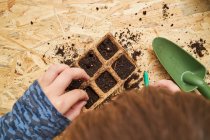 From above of crop anonymous kid with seed dispenser digging holes in biodegradable container with soil — Stock Photo