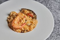 Сверху аппетитный рис с разнообразными морепродуктами подается на тарелке на столе в ресторане — стоковое фото