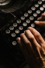 Зверху знімок рук анонімної людини, що друкує на клавіатурі старовинної друкарської машинки — стокове фото