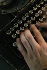 Сверху снимок рук анонимного человека, печатающего на клавиатуре винтажной пишущей машинки — стоковое фото