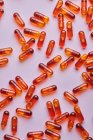 Вид зверху композиція помаранчевих таблеток, розкиданих на рожевому фоні в світлій студії — стокове фото