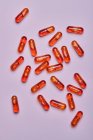 Вид зверху композиція помаранчевих таблеток, розкиданих на рожевому фоні в світлій студії — стокове фото