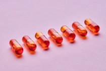 Composición de vista superior de píldoras de color naranja sobre fondo rosa en estudio de luz - foto de stock