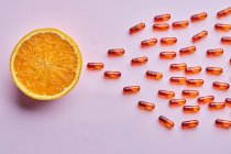 Zusammensetzung reifer geschnittener Orangen auf rosa Oberfläche in der Nähe verstreuter Pillen im Lichtstudio — Stockfoto