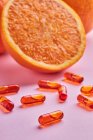 Состав спелых срезанных апельсинов, расположенных на розовой поверхности возле разбросанных таблеток в светлой студии — стоковое фото