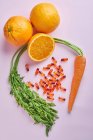 Сверху композиция разбросаны витамины таблетки расположены на розовом столе возле спелых моркови и сочных апельсинов — стоковое фото