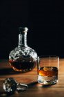 Glas kalten Whiskys mit Eis auf Holztisch in der Nähe der Karaffe auf schwarzem Hintergrund — Stockfoto