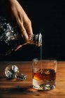 Glass of cold whiskey with ice placed on wooden table near decanter on black background — Stock Photo