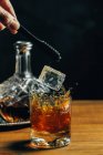 Bicchiere di whisky freddo con ghiaccio posto su tavolo di legno vicino decanter su sfondo nero — Foto stock