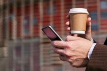Вид збоку врожаю невпізнаваний сіроволосий бородатий чоловік у формальному костюмі, що п'є каву та перегляд мобільного телефону на міській вулиці — стокове фото