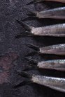 Recorte vista de cerca de las colas de anchoas crudas que yacen en la superficie oscura - foto de stock