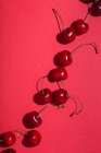 De acima mencionadas cerejas apetitosas vermelhas brilhantes com hastes no fundo rosa — Fotografia de Stock