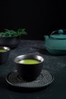 Черная керамическая чашка с традиционным японским зеленым чаем маття подается на стол с чайником — стоковое фото