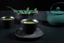 Черная керамическая чашка с традиционным японским зеленым чаем маття подается на стол с чайником — стоковое фото
