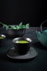 Black ceramic cup with traditional Japanese green colored matcha tea served on table with teapot — Stock Photo