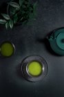 Чорна керамічна чашка з традиційним японським зеленим кольором мача чай подається на столі з чайником. — стокове фото