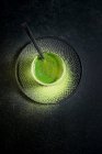 Dall'alto di sano tè verde matcha alle erbe servito in tazza di vetro con decorazione in metallo sul piattino cosparso di polvere sul tavolo nero — Foto stock