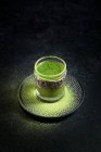 From above of healthy herbal green matcha tea served in glass cup with metal decoration on saucer sprinkled with powder on black table — Stock Photo