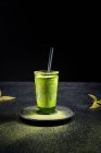 Sano tè verde matcha alle erbe servito in tazza di vetro con decorazione in metallo sul piattino cosparso di polvere sul tavolo nero — Foto stock