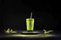 Thé matcha vert à base de plantes sain servi dans une tasse en verre avec décoration en métal sur une soucoupe saupoudrée de poudre sur une table noire — Photo de stock