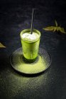 Angolo alto di vetro con caffè matcha verde freddo con latte servito con paglia sul piattino sul tavolo nero — Foto stock