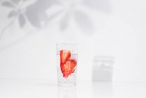 Eau saine et rafraîchissante infusée de désintoxication aux fraises fraîches coupées en tranches, servie en verre transparent contre un mur blanc ombragé — Photo de stock