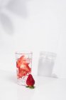 Здоровый освежающий детоксикации воды с свежей спелых нарезанных клубники подается в прозрачном стекле против белой стены с тенями — стоковое фото