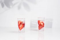 Refreshing summer drink with fresh sliced strawberries and ice cubes with water served in glasses on white table — Stock Photo
