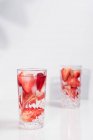 Refreshing summer drink with fresh sliced strawberries and ice cubes with water served in glasses on white table — Stock Photo