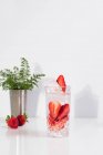 Освежающий летний напиток со свежей клубникой и кубиками льда с водой, подаваемой в стакане на белом столе — стоковое фото