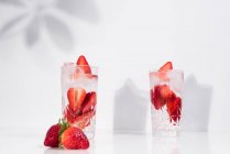 Bebida refrescante de verão com morangos fatiados frescos e cubos de gelo com água servida em copos na mesa branca — Fotografia de Stock