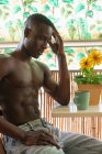 Боковой вид безрубашечного вдумчивого афроамериканского мужчины, демонстрирующего мускулы дома и отворачивающегося — стоковое фото